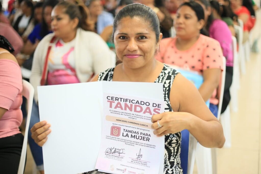 Mujer tabasqueña sostiene su certificado del programa Tandas para la Mujer en evento comunitario.