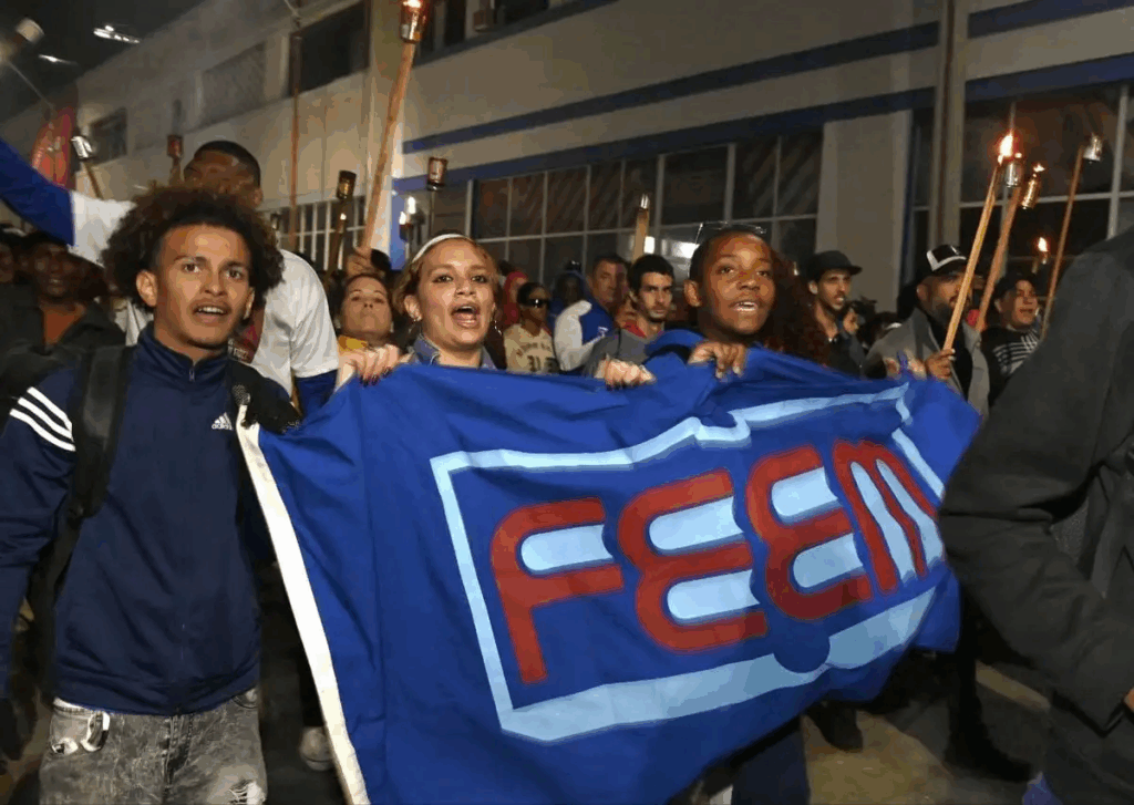 Jóvenes cubanos sostienen bandera de la FEU y antorchas durante marcha nocturna en La Habana.