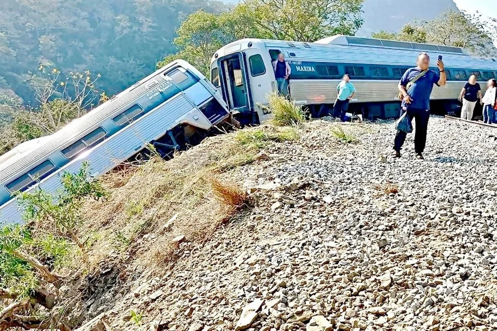 Dos vagones del Tren Interoceánico descarrilados sobre balastro en zona montañosa mientras pasajeros descienden.
