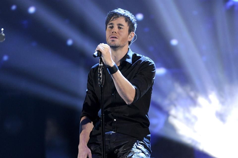 Enrique Iglesias cantando en un escenario iluminado, sosteniendo el micrófono durante una presentación en vivo.