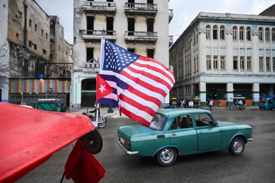Banderas de Cuba y Estados Unidos colocadas sobre un vehículo frente al Capitolio de La Habana bajo cielo nublado.