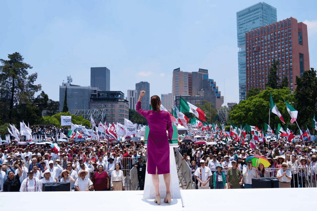 La presidenta Claudia Sheinbaum de espaldas frente al pódium, con el puño derecho en alto, ante la multitud congregada en el Monumento a la Revolución durante el mitin del 1 de junio de 2025